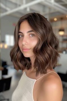 Woman with shoulder-length wavy brown hair in a bright, modern room. All Over Natural Brown Hair Color, Chocolate Brown Medium Hair, Medium Bob Brown Hair, Dark Brown To Chocolate Brown Hair, Glaze On Brown Hair, Neutral Tone Brown Hair, Chestnut Brown Hair Short, Chocolate Glaze Hair Color, Neutral Medium Brown Hair