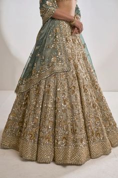 a woman in a gold and green lehenga with an intricate design on the skirt