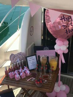 a table filled with pink and white balloons next to a wooden table topped with drinks