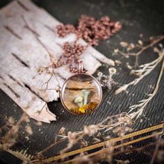 a necklace with a bird on it sitting on top of a piece of wood next to dried flowers