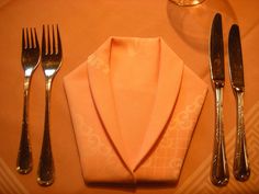 silverware and utensils are laid out on a place mat with an orange napkin