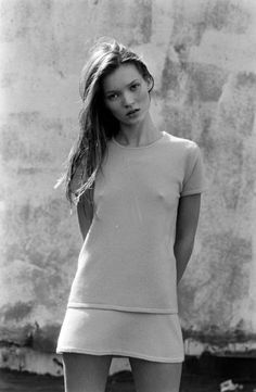 black and white photograph of a woman in short shorts standing next to a concrete wall