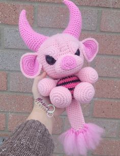 a hand holding a pink stuffed animal in front of a brick wall