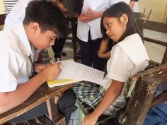 two young children sitting at desks writing on paper