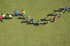 a group of people holding hands in the shape of a heart on top of grass