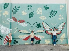 three people standing in front of a painted wall with butterflies and ladybugs on it