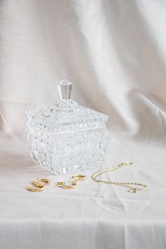 a clear glass container sitting on top of a white cloth next to two gold rings