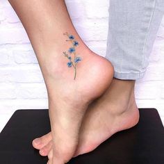 a woman's foot with a small blue flower tattoo on her left side ankle