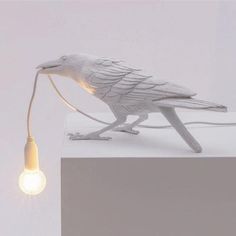 a white bird lamp sitting on top of a table next to a small light bulb