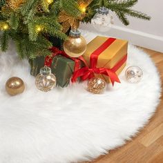 a christmas tree with presents under it on a white rug next to a gold and red present box