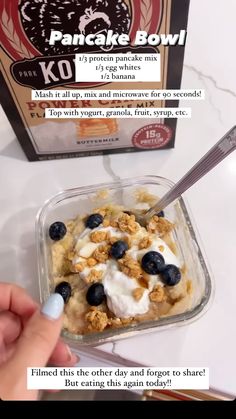 a person is holding a spoon over a bowl of food with yogurt and blueberries