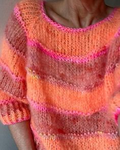 an older woman is wearing a pink and orange striped knitted sweater, with her hands in her pockets