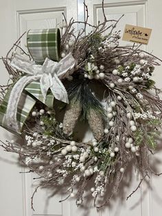 a wreath is hanging on the door with white flowers and green ribbon around it,