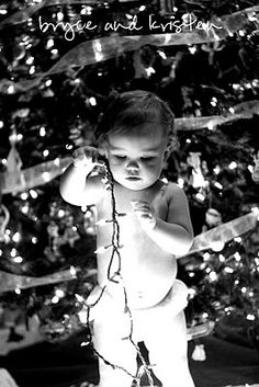 a baby standing in front of a christmas tree with lights on it's head