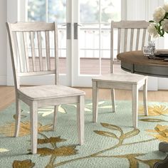 two wooden chairs sitting on top of a rug next to a table with flowers in it