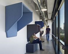 a man sitting on top of a blue bench next to a tall window in an office building