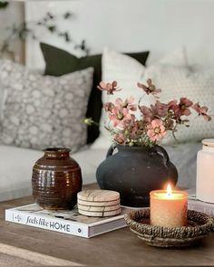 a coffee table with candles, books and flowers on it in front of a couch