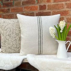 a white vase filled with flowers sitting on top of a bench next to a brick wall