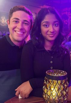 a man and woman sitting at a table in front of a vase with lights on it