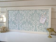 a white frame with a blue damask pattern on it and a small bird figurine next to it