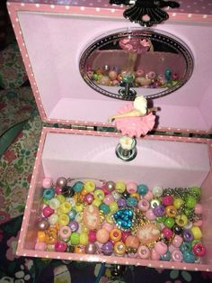 an open pink box filled with lots of colorful beads and buttons on top of a table