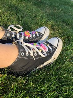 a person's feet wearing black and white converse sneakers on green grass with pink flowers