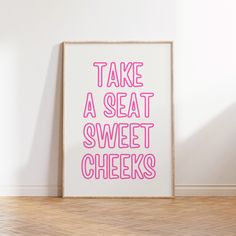 a pink print that says, take a seat sweet cheeks on the floor in front of a white wall