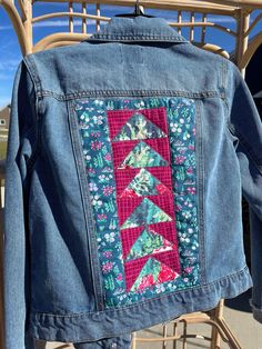 a jean jacket is hanging up on a chair with flowers and trees embroidered on it