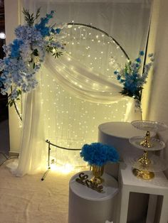 blue flowers and candles are on display in front of a white drapeed curtain