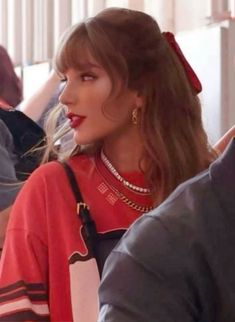 a woman with long hair and red lipstick sitting in front of other people at an event