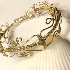 a close up of a gold bracelet on a white seashell with a sea urn in the background