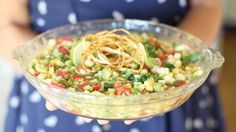 a woman is holding a bowl full of food with noodles and veggies in it