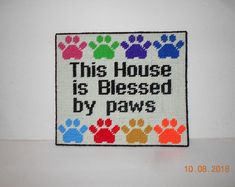 this house is based by paws cross stitched onto a white background with multicolored paw prints