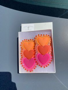 two pink and orange heart shaped earrings in a box on top of a car dashboard