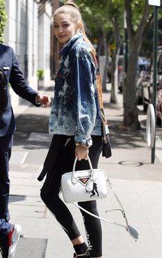 a woman is walking down the street carrying a white handbag and wearing black leggings