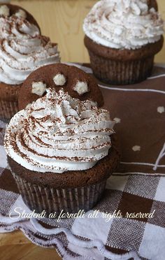 three cupcakes with white frosting on a brown and white checkered cloth