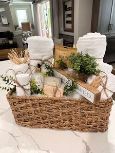 a wicker basket filled with white towels and greenery on top of a table