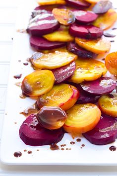 sliced up beets and carrots on a white cutting board with brown sauce drizzled over them