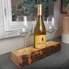 a bottle of wine sitting on top of a wooden block next to two glasses and a potted plant