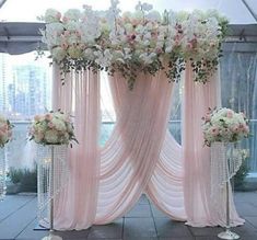 an outdoor wedding setup with pink drapes and white flowers on the side, in front of a large window