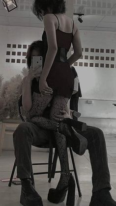 a woman sitting on top of a chair next to a man holding a cell phone