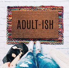 a person sitting in front of a door with their feet up on the floor, next to a welcome mat that reads'the dog toys are part of the decor '