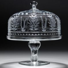 a clear glass cake dish with an ornate design on the top and bottom, under a domed glass cover