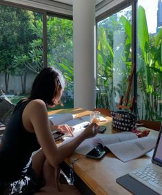 a woman sitting at a desk in front of a laptop computer with an open book on it