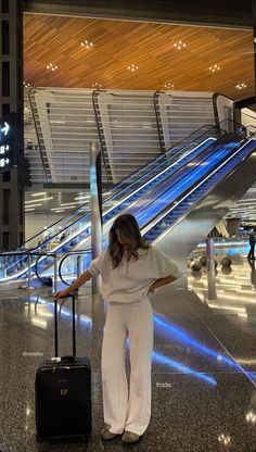 a woman standing in an airport with her luggage and looking at the escalator