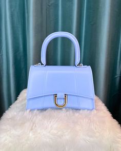 We LOVE this baby blue mini rubbery top handle bag with gold hardware. It's large enough to fit the essentials, but small enough to not weigh you down. (crossbody chain included) - Made of 100% polyvinyl chloride 9" H x 7.5" W x 3.5" D Light Blue Top Handle Shoulder Bag With Detachable Handle, Chic Light Blue Shoulder Bag With Top Carry Handle, Chic Light Blue Shoulder Bag With Top Handle, Light Blue Top Handle Satchel With Carry Handle, Trendy Light Blue Bag With Detachable Handle, Blue Handheld Bag With Gold-tone Hardware, Blue Handheld Bags With Gold-tone Hardware, Blue Handheld Satchel With Adjustable Handle, Blue Top Handle Satchel With Adjustable Handle