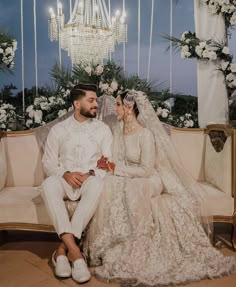 a bride and groom sitting on a couch in front of a chandelier