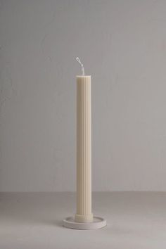 a white pillar with a candle in the middle on a grey surface, against a plain background