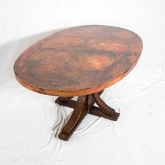 an old round wooden table sitting on top of a white sheet