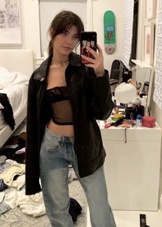 a woman taking a selfie in her bedroom with clothes on the floor and bed behind her